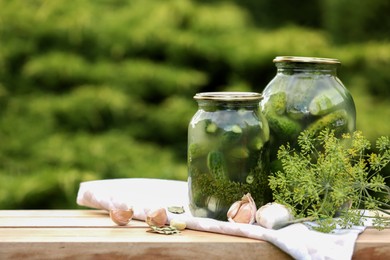 Jars of delicious pickled cucumbers and ingredients on wooden table against blurred background. Space for text