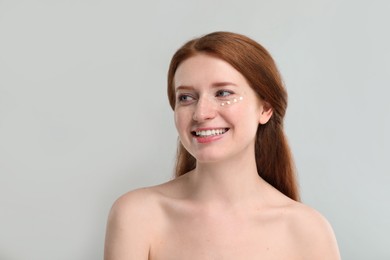 Photo of Smiling woman with freckles and cream on her face against grey background