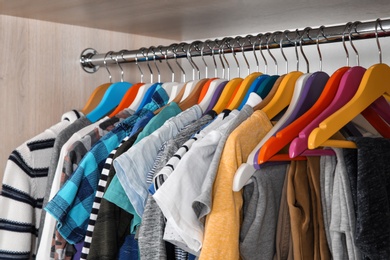 Photo of Stylish boy's clothes hanging in wardrobe, closeup