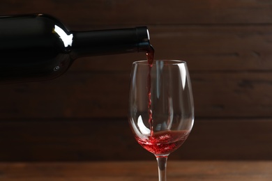 Photo of Pouring delicious red wine into glass on blurred background