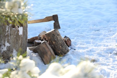 Metal axe in wooden log and pile of wood outdoors on sunny winter day. Space for text