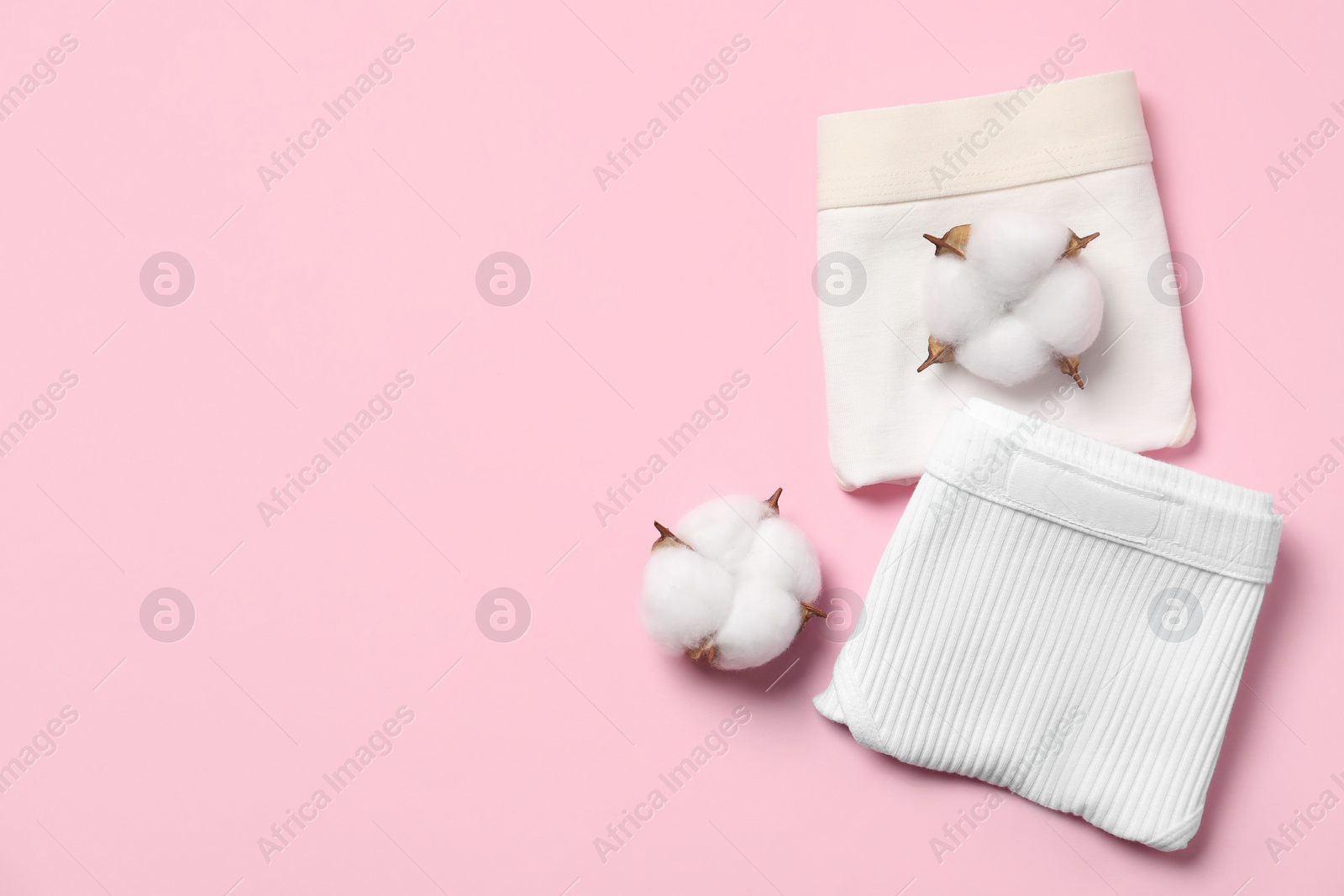 Photo of Stylish folded women's underwear and cotton flowers on pink background, flat lay. Space for text