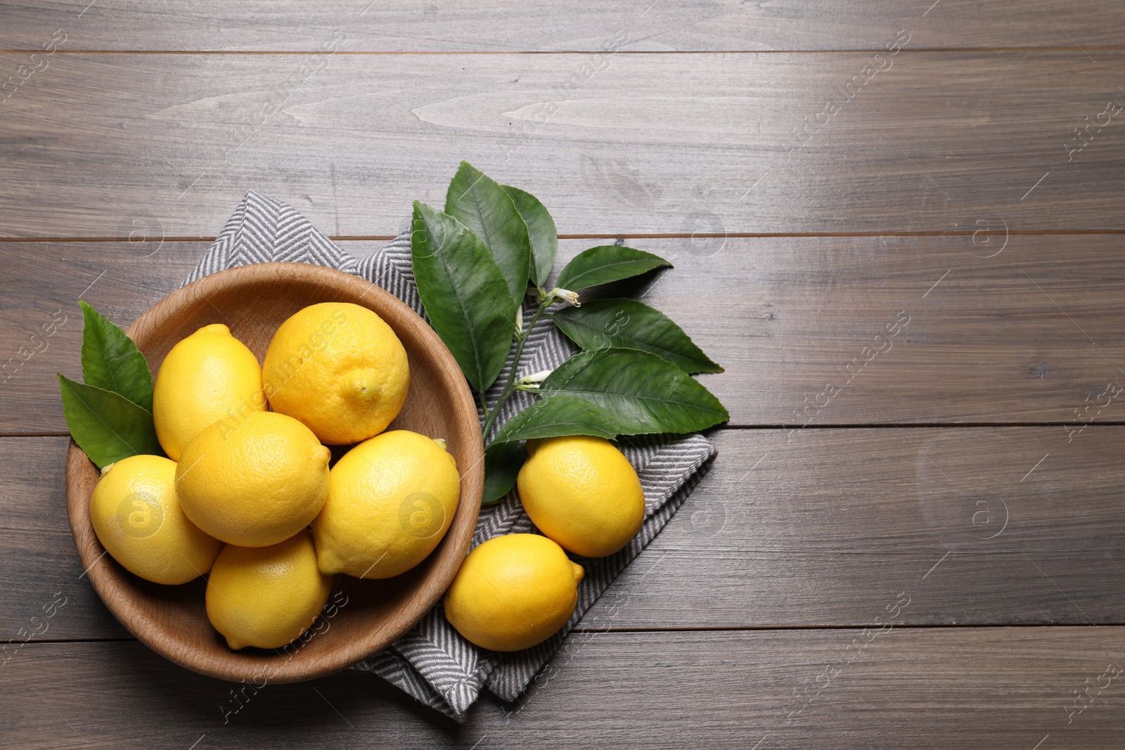 Photo of Many fresh ripe lemons with green leaves on wooden table, flat lay. Space for text