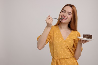 Photo of Young woman eating piece of tasty cake on light grey background, space for text