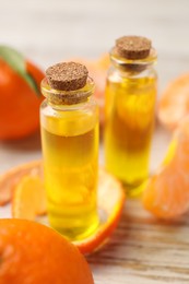Photo of Bottles of tangerine essential oil, fresh fruits and peel on white wooden table, closeup