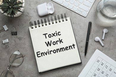 Image of Notebook with text Toxic Work Environment on grey table, flat lay