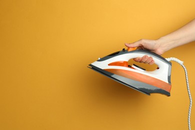 Photo of Woman holding modern iron on orange background, closeup. Space for text