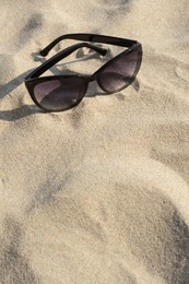 Photo of Stylish sunglasses with black frame on sandy beach, space for text