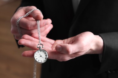 Man holding chain with elegant pocket watch on blurred background, closeup