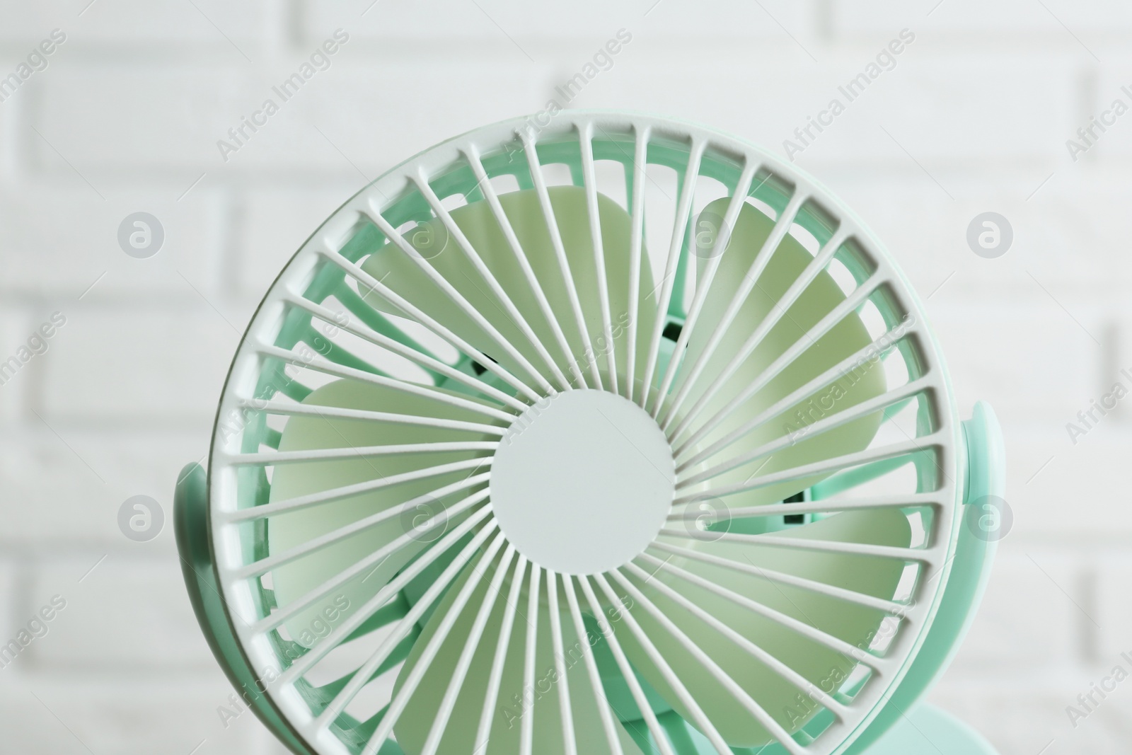 Photo of Portable fan near white brick wall, closeup. Summer heat