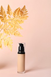 Photo of Bottle of skin foundation and decorative plant on beige background. Makeup product