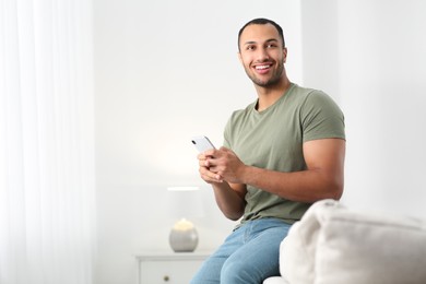 Photo of Smiling African American man with smartphone on sofa at home. Space for text