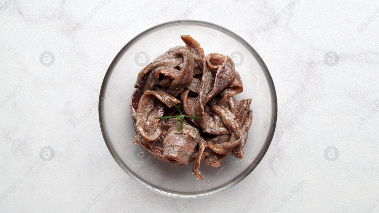 Photo of Canned anchovy fillets in glass bowl on white marble table, top view