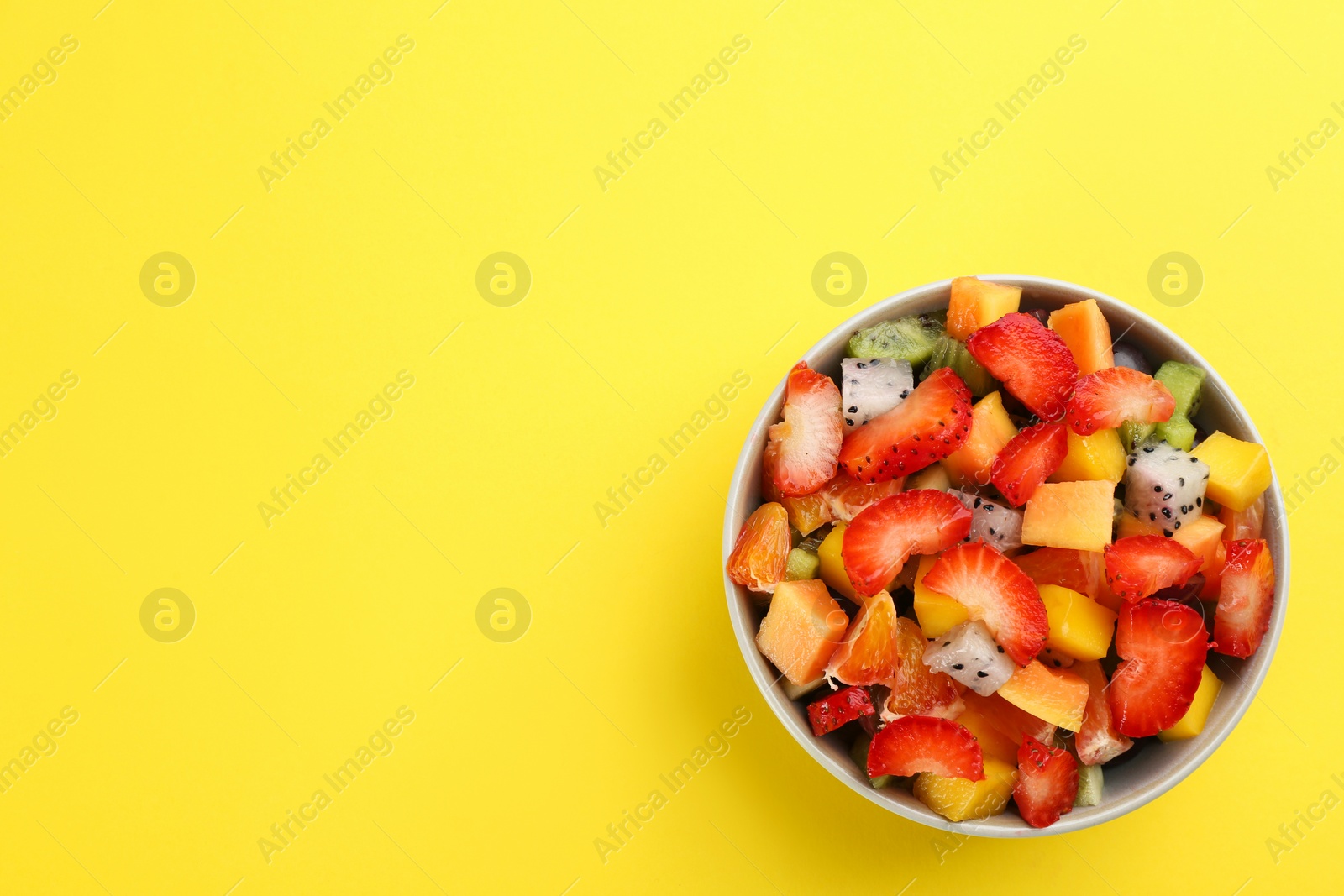 Photo of Delicious exotic fruit salad on yellow background, top view. Space for text