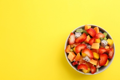 Photo of Delicious exotic fruit salad on yellow background, top view. Space for text