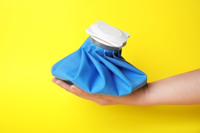 Woman holding ice pack against yellow background, closeup