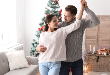 Happy young couple dancing near Christmas tree at home