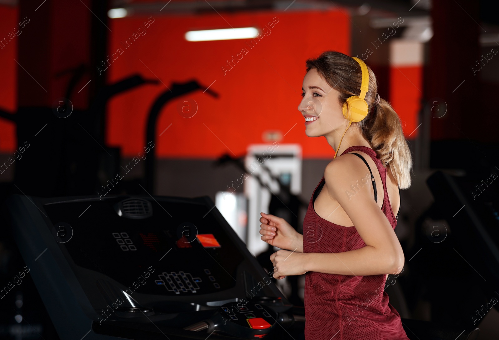 Photo of Young woman with headphones listening to music and running on treadmill at gym