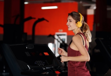 Photo of Young woman with headphones listening to music and running on treadmill at gym