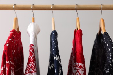 Rack with different Christmas sweaters on light background, closeup