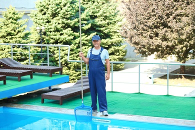 Male worker cleaning outdoor pool with scoop net