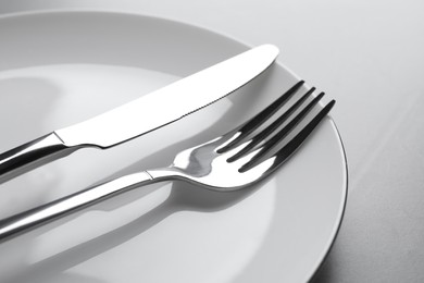 Photo of Plate with fork and knife on light grey table, closeup