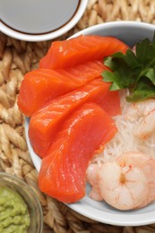 Delicious sashimi set of salmon and shrimps served with funchosa, parsley, wasabi and soy sauce on wicker mat, flat lay