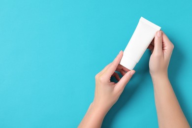 Woman with tube of hand cream on light blue background, top view. Space for text