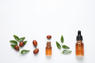 Photo of Glass bottles with jojoba oil and seeds on white background, top view