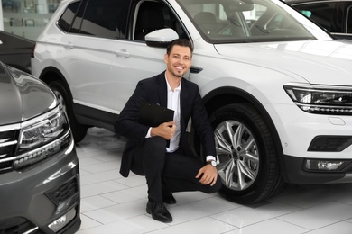 Salesman with clipboard near new car in salon