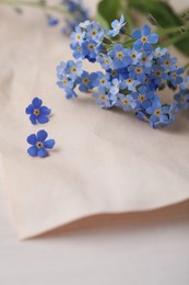 Photo of Beautiful Forget-me-not flowers and parchment on white wooden table, closeup
