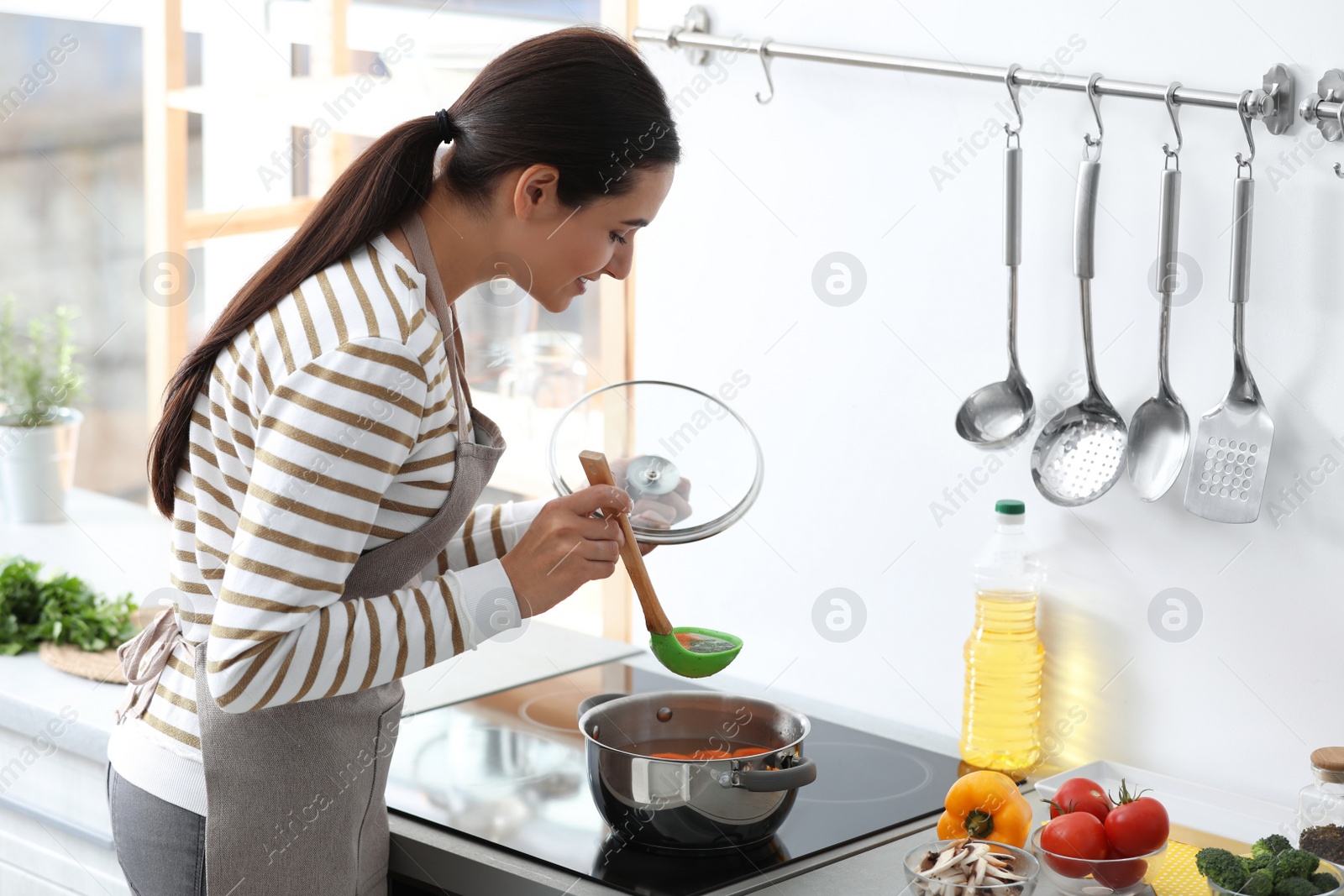 Photo of Young woman cooking tasty soup in kitchen