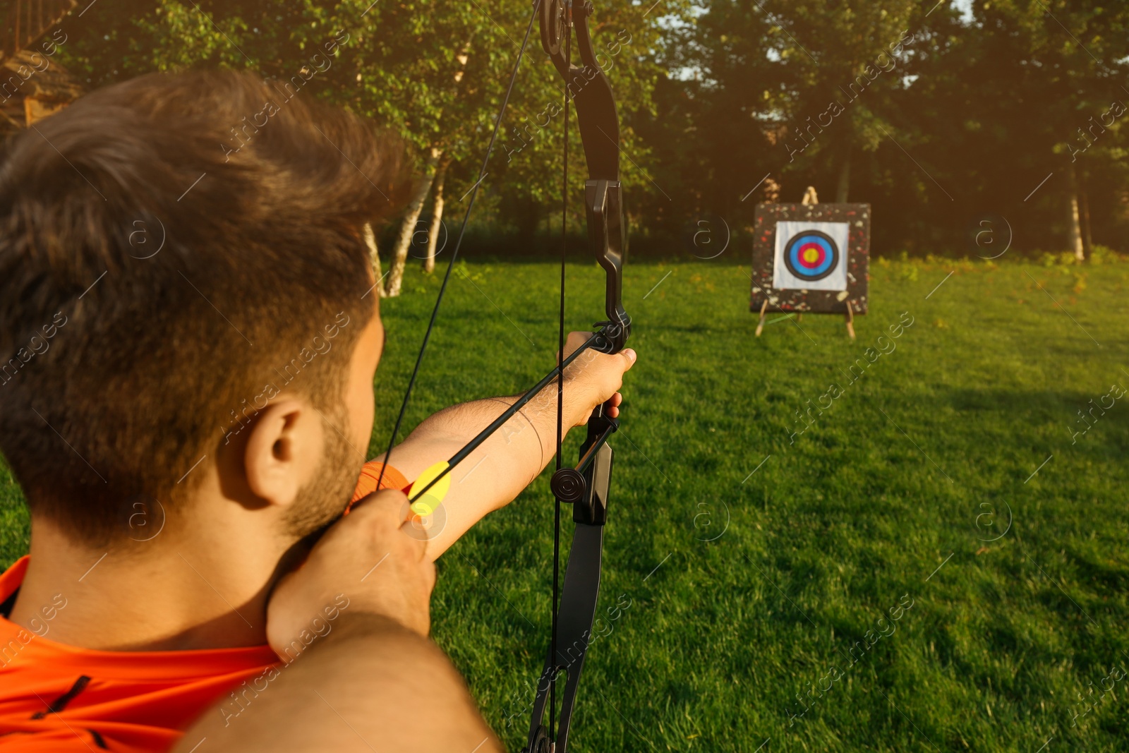 Photo of Man with bow and arrow aiming at archery target in park, back view