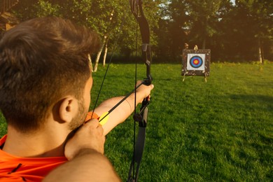 Man with bow and arrow aiming at archery target in park, back view