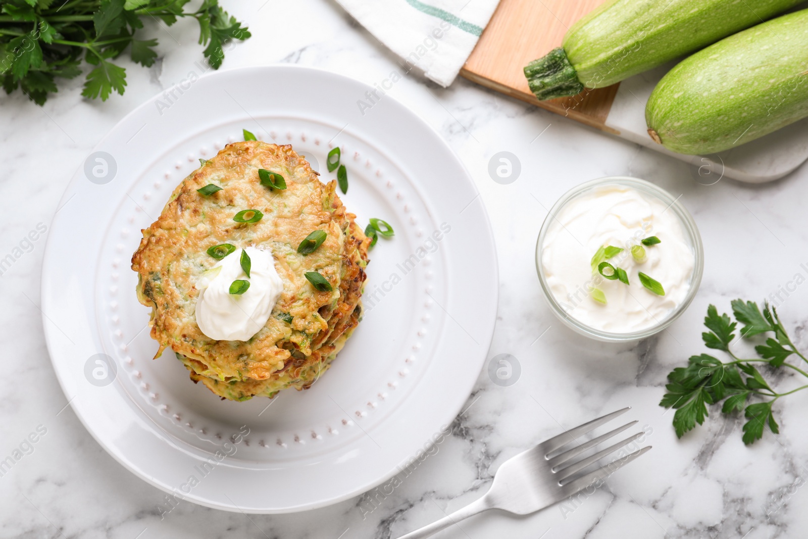 Photo of Delicious zucchini fritters served on white marble table, flat lay