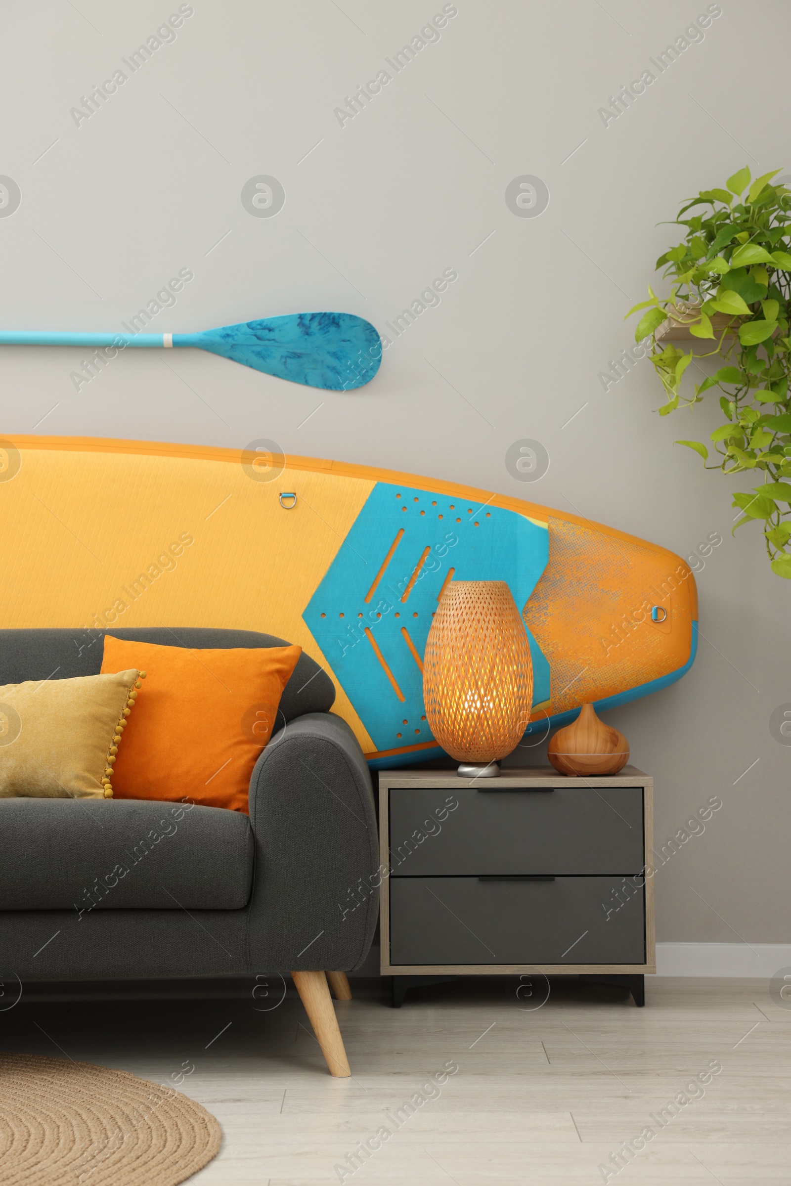 Photo of SUP board, paddle and stylish sofa in living room. Interior design