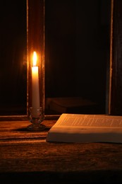 Photo of Burning candle and Bible on wooden table near window at night