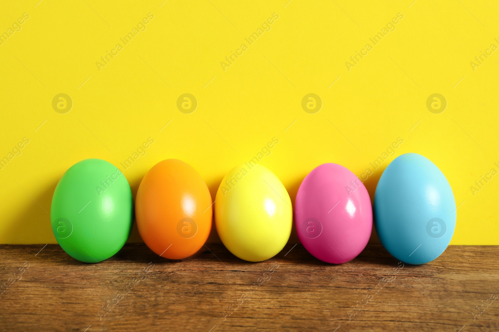 Photo of Easter eggs on wooden table against yellow background