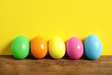 Photo of Easter eggs on wooden table against yellow background