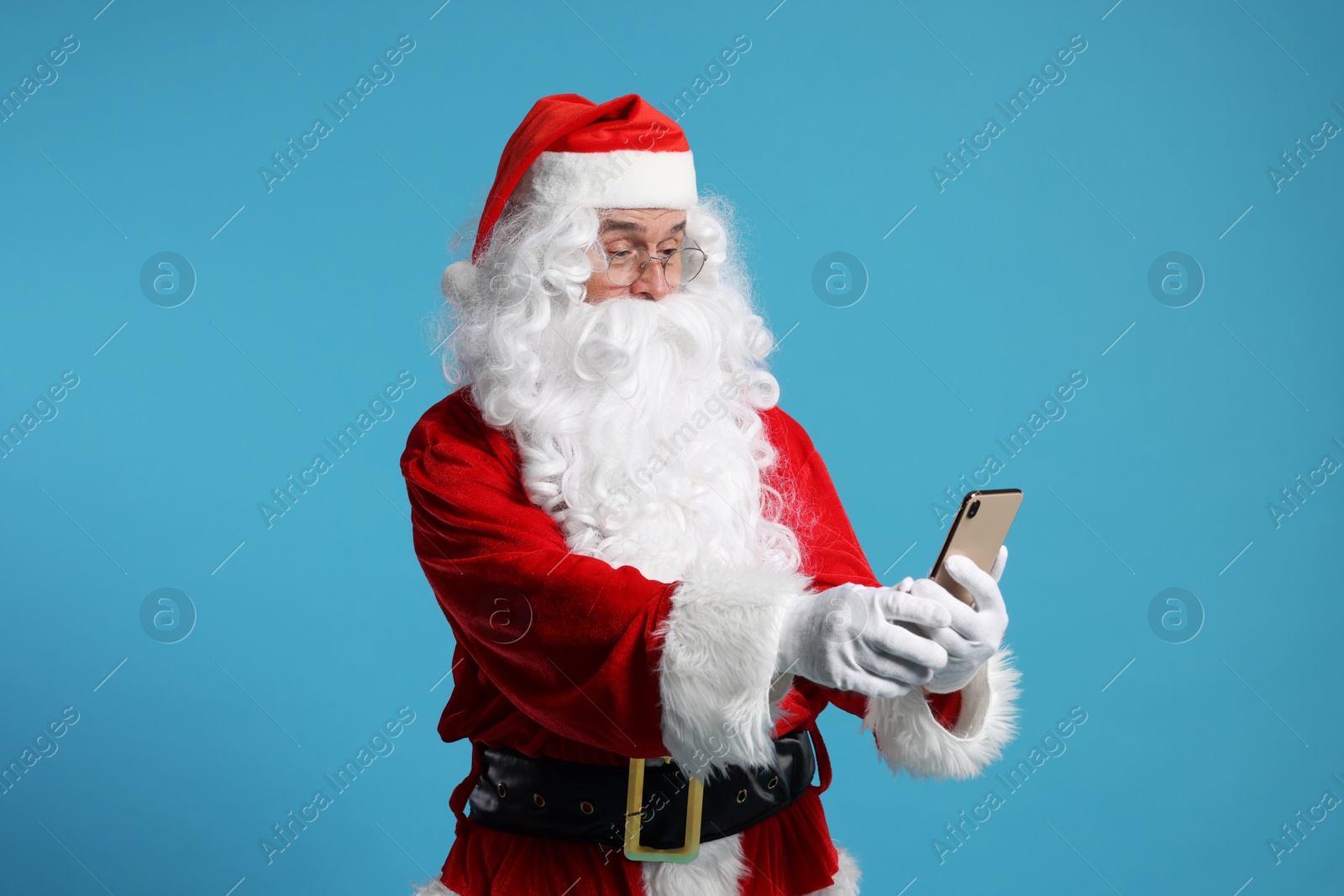 Photo of Merry Christmas. Santa Claus using smartphone on light blue background