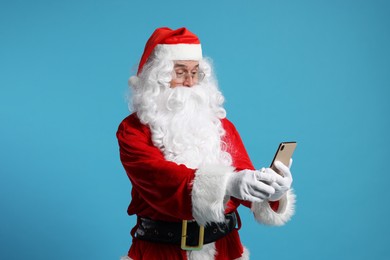 Merry Christmas. Santa Claus using smartphone on light blue background
