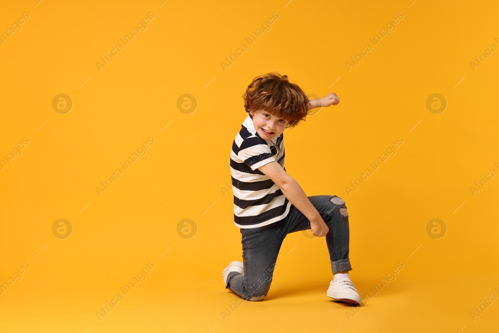 Photo of Happy little boy dancing on yellow background. Space for text