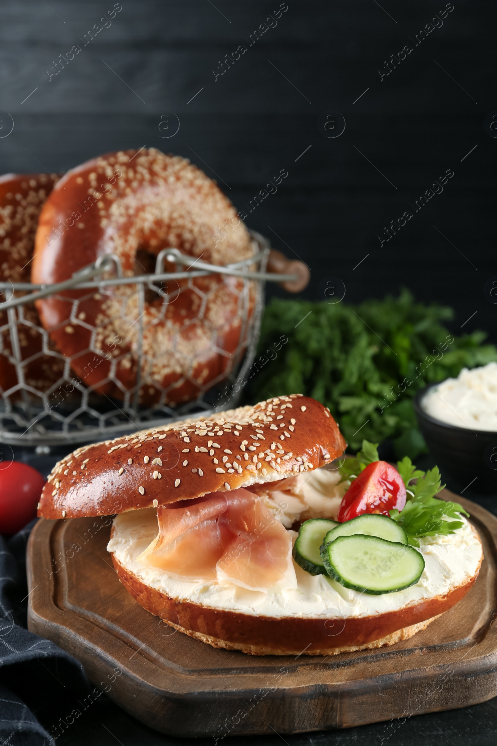 Photo of Delicious bagel with cream cheese, jamon, cucumber, tomato and parsley on black table