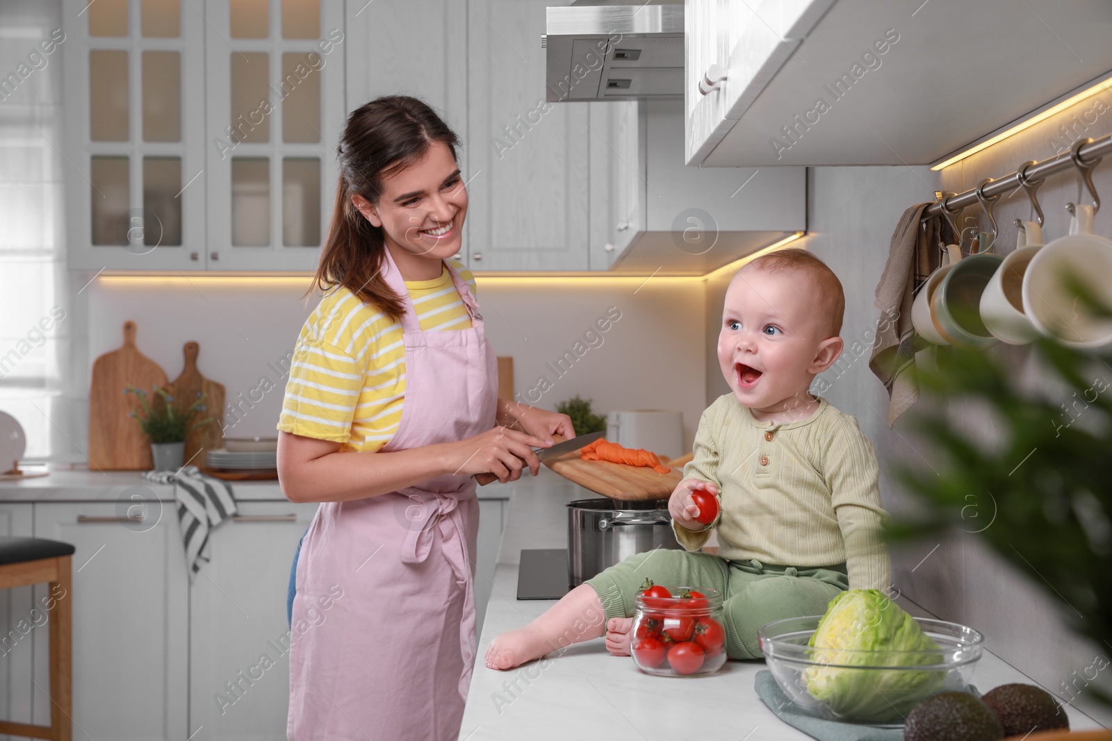 Photo of Happy young woman with her cute baby spending time together in kitchen