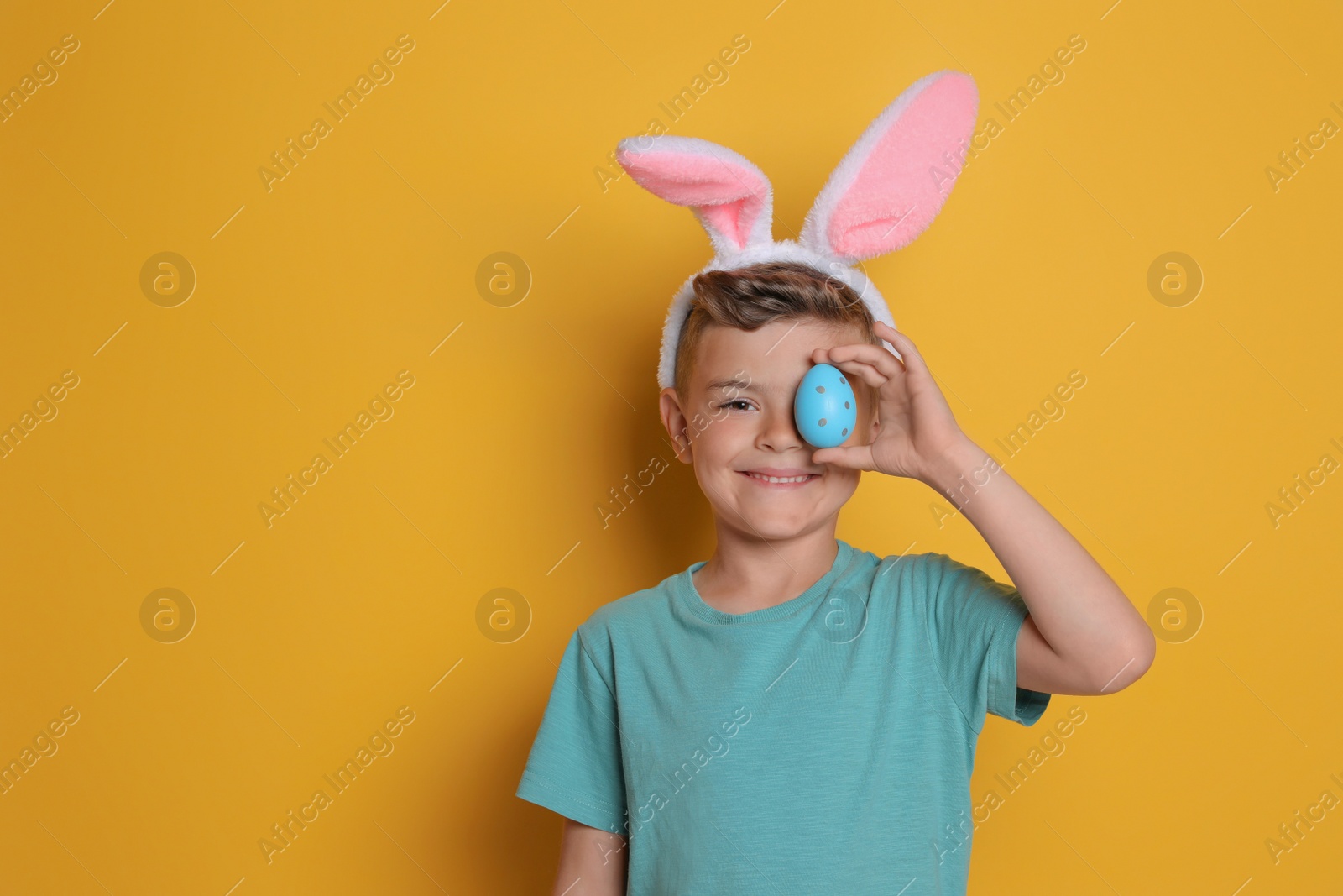 Photo of Cute little boy in bunny ears holding Easter egg on yellow background