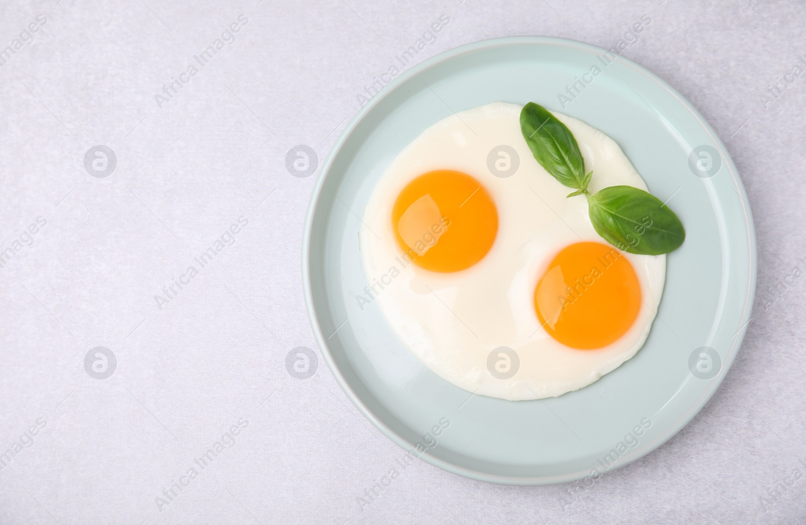 Photo of Tasty fried eggs with basil in plate on white table, top view. Space for text