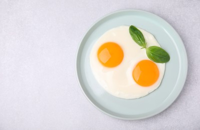 Tasty fried eggs with basil in plate on white table, top view. Space for text