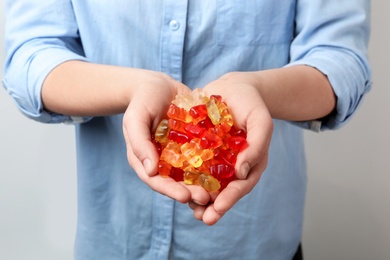 Woman holding colorful jelly bears on light background, closeup