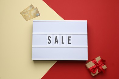 Lightbox with word Sale, gift box and credit cards on color background, flat lay