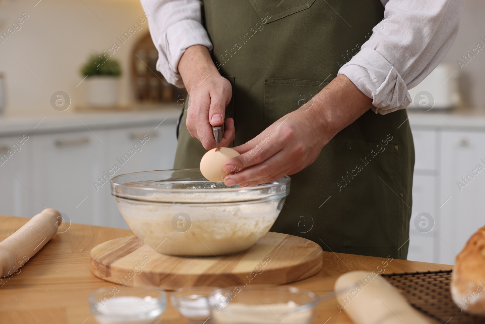 Photo of Making bread. Man putting raw egg into dough at wooden table in kitchen, closeup